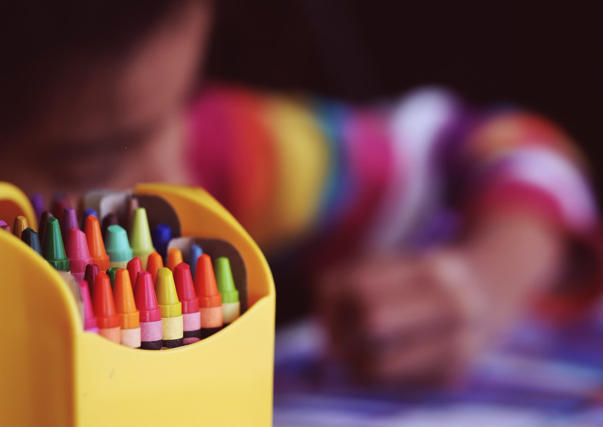 An image of a pack of crayons with a child in the background.