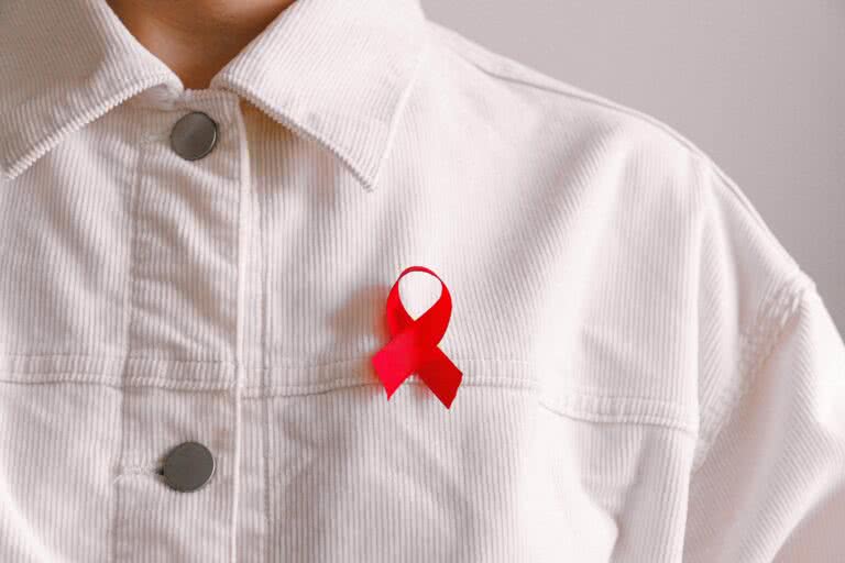 A person wearing a red AIDS awareness ribbon on their shirt