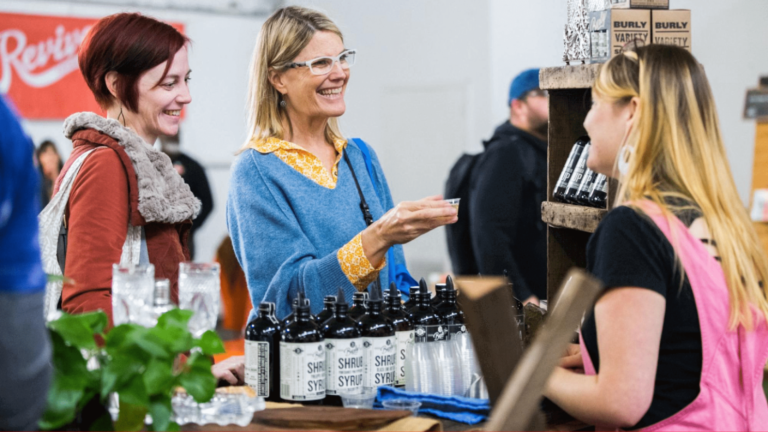 Two people trying syrup from a food vendor at an event