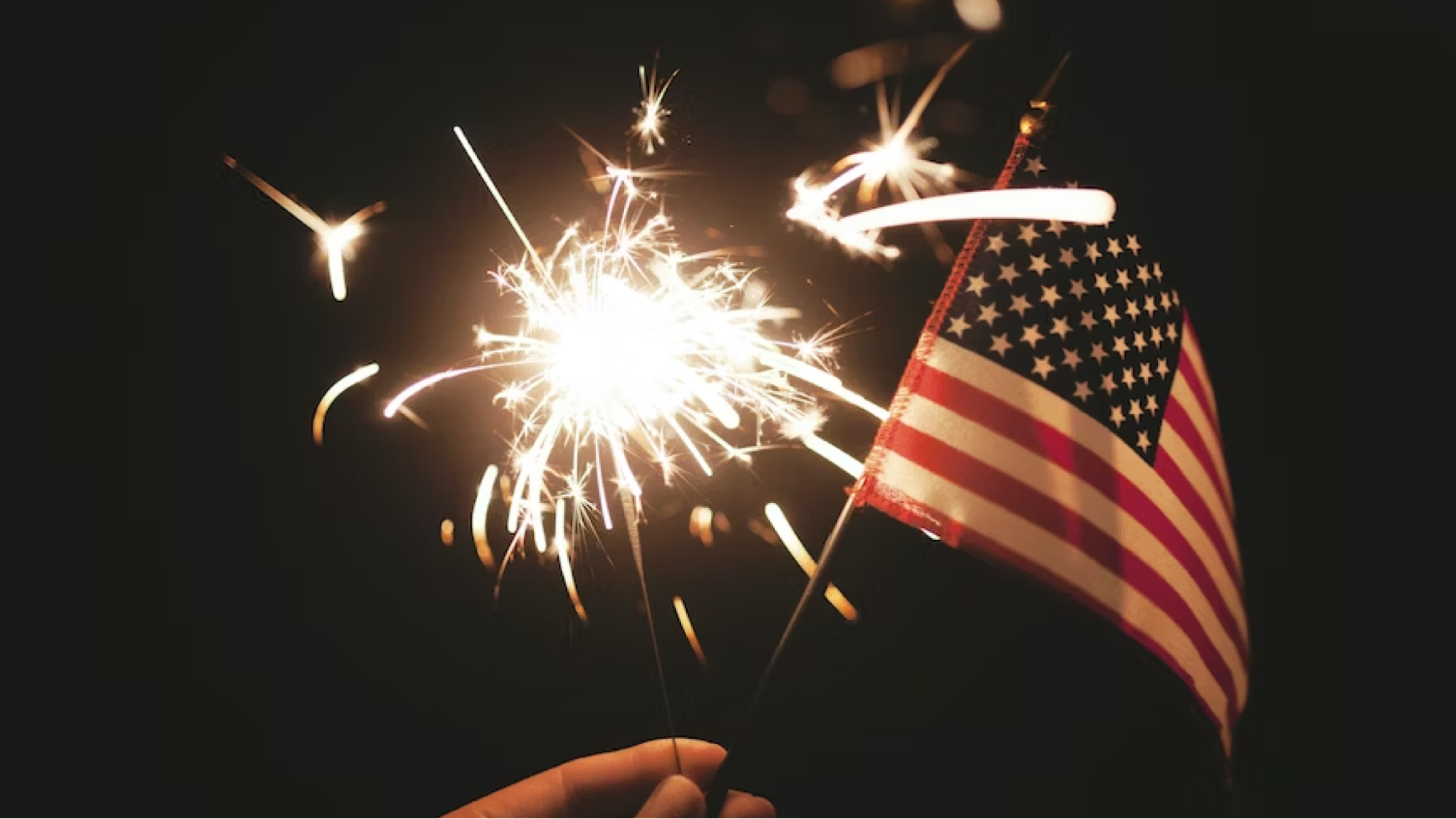 Person holds small American flag and a lit sparkler