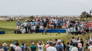 A golfer tees off while a crowd watches