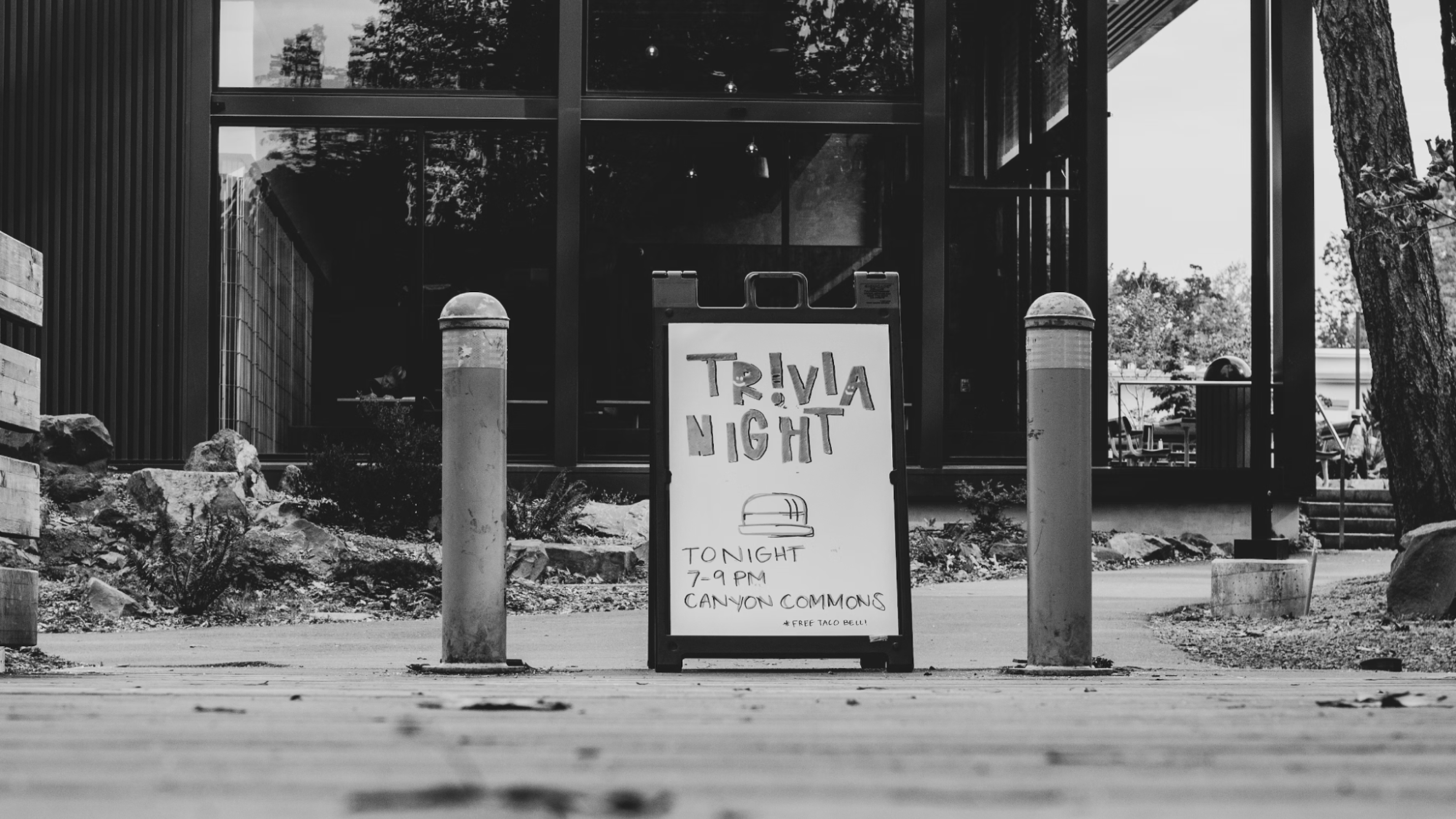 Black and white photo of a sign in the street promoting a trivia night