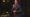 Man stands on stage smiling while talking into mic